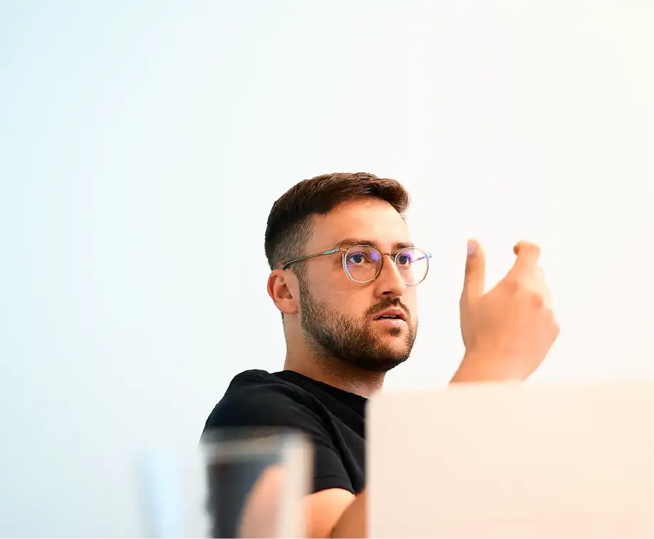 Mann mit Brille gestikuliert im Gespräch, unscharfer heller Hintergrund